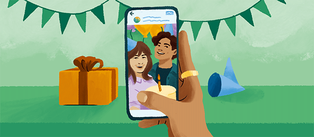 A hand is holding a phone. There are party decorations in the background. On the phone are two people holding a cake.